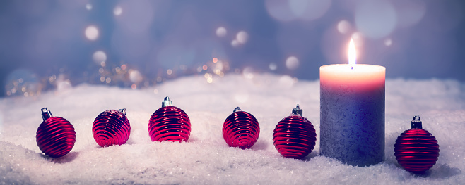 shiny candle light and red balls in a row on snowy christmas background, beautiful christmas decoration concept