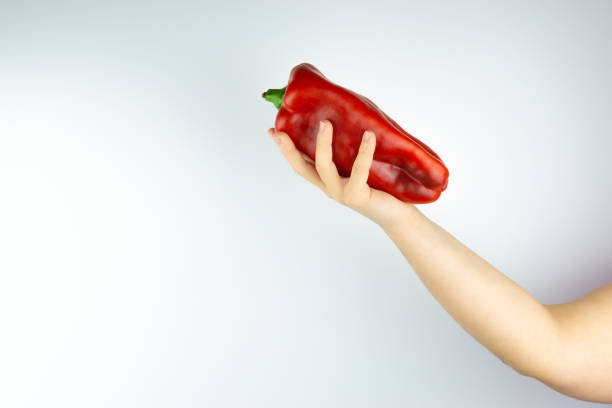istock Woman's arm holding a red pepper with her hand on a white background 1286100503