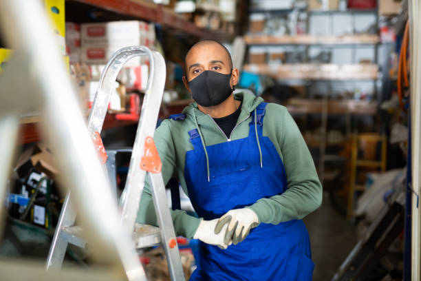 istock Warehouse worker in protective mask stands next to stepladder and tool shelves in hardware store 1286103614