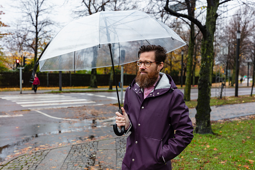 Stylish groom and groomsmen standing under black umbrella and posing. Confident man in suit holding umbrella in rainy outdoors. Rich Businessman. Finance wealth and business