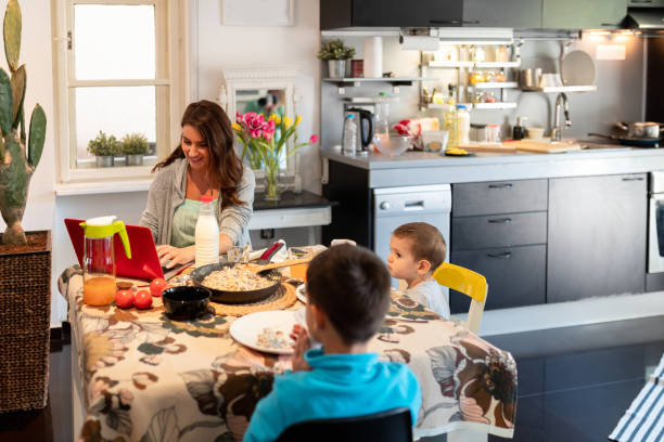 istock Happy mother working on laptop at the dining table, sons having lunch 1286112331