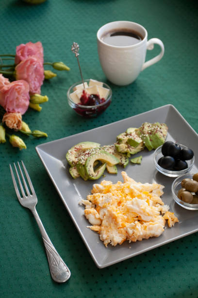 istock Nutritious breakfast per person: scrambled eggs, olives, olives, avocados, cheese and raspberry jam. Next to it is a cup of black coffee and a bouquet of flowers. 1286113020