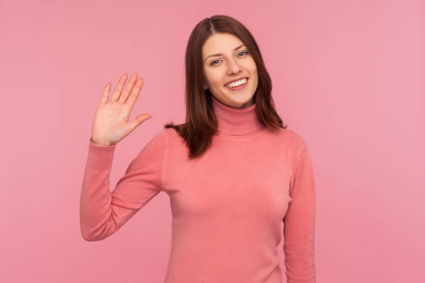 amigable mujer positiva con el pelo castaño agitando su mano mostrando hi gesto, dando la bienvenida y saludando - waving arms fotografías e imágenes de stock