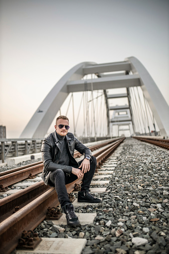 Photo of fashion young man sitting on railway