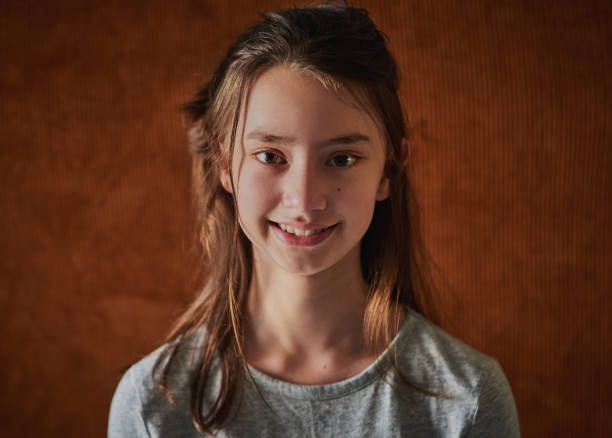 Portrait of a cute young girl standing against a brown background