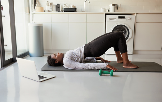 Shot of a young woman using a laptop while exercising at home