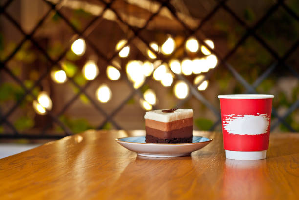 Red cup with a cake on a wooden board. Disposable coffee cup on a brown table. Place for text on the cup. Layout for design.