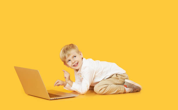 istock Litttle child boy using laptop on yellow background. Education, online study, home studying, distance learning. Primary school student during quarantine 1286121351