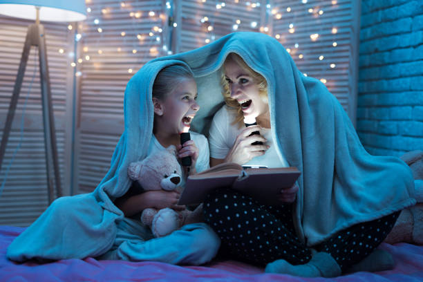 Grandmother and granddaughter are reading fairy tales under blanket at night at home. stock photo