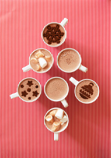 istock Cups with hot chocolate with marshmallows and cocoa powder decor in white mugs on white red striped wrapped paper background stay Christmas tree shape, top view 1286122048