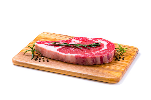 High angle view close-up of a meat chop with pepper and rosemary on a wooden cutting board isolated on white background. Studio shot taken with Canon EOS 6D Mark II and Canon EF 100 mm f/ 2.8