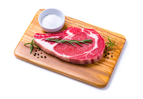 High angle view close-up of a meat chop with salt, pepper and rosemary on a wooden cutting board isolated on white background. Studio shot taken with Canon EOS 6D Mark II and Canon EF 100 mm f/ 2.8