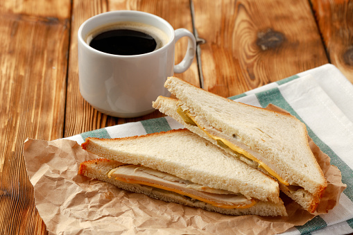 Toasted sandwich in craft paper with cup of coffee on table clsoe up