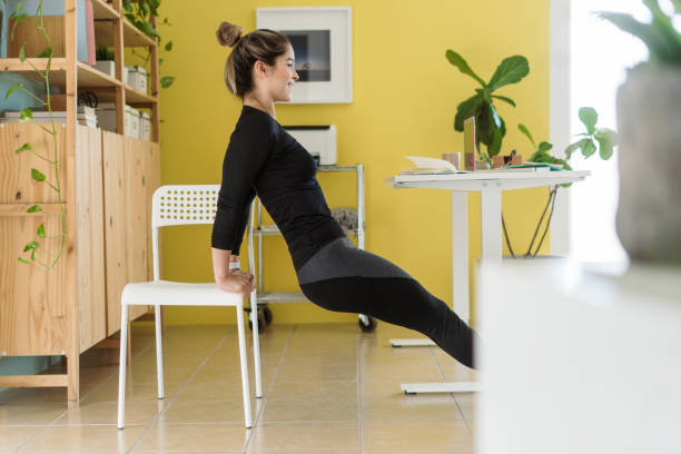 Happy young woman exercising with chair at work A happy young latin woman exercising with a chair at work and smiling. Proper Posture and Movement stock pictures, royalty-free photos & images