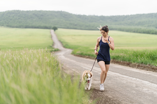 A cute young latin woman and her dog walking on a road in the countryside.