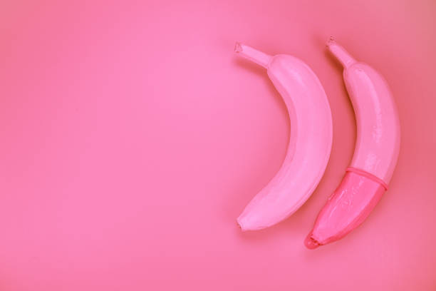 abstract photography of bananas with condom with pink background - sex education condom contraceptive sex imagens e fotografias de stock