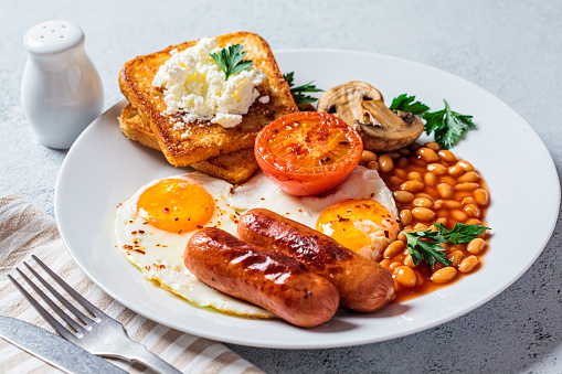 English breakfast with sausages, beans, fried eggs, toast, mushrooms and tomatoes in a white plate. English breakfast concept.