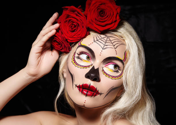 Beautiful Halloween Make-Up Style. Blond Model Wear Sugar Skull Makeup with Red Roses. Santa Muerte concept Beautiful Halloween Make-Up Style. Blond Model Wear Sugar Skull Makeup with Red Roses, pale Skin Tones and Waves Hair. Santa Muerte concept muerte stock pictures, royalty-free photos & images