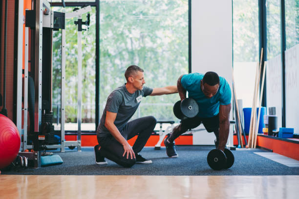 Workout with male personal trainer in health club Sportsman in plank position exercising dumbbell push-ups fitness instructor stock pictures, royalty-free photos & images