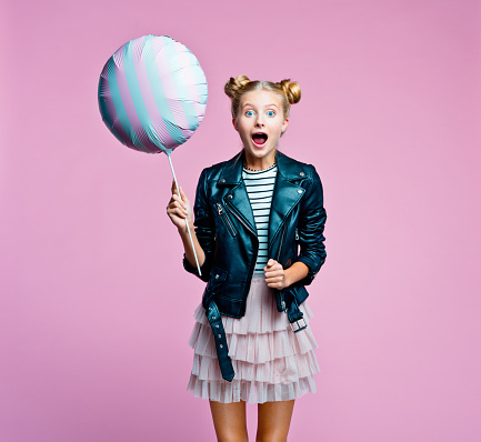 Cute female teenager wearing black leather jacket and pink tulle skirt holding big balloon. Smiling girl going to the party. Studio shot on pink background.