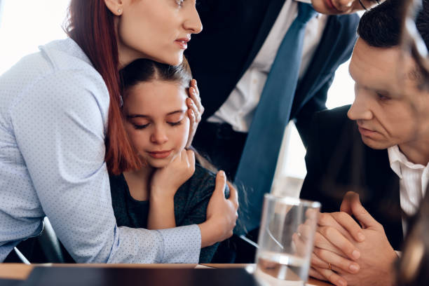 Young red-haired woman hugging crying girl. Man in suit tries to calm mother and daughter. stock photo