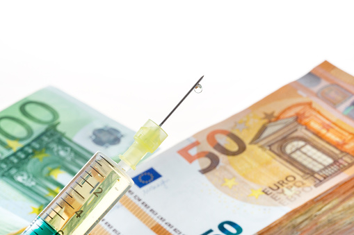Syringe, vaccine and euro banknotes - concept of costs of health care. Corona pandemic.