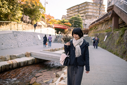 Young woman visiting Kobe Arima Onsen (hot spa) district for solo trip in autumn season to enjoy beautiful scenery of traditional Japanese village and tasty foods and local saki (Japanese rice wine).