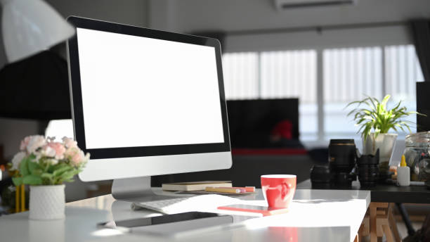 Contemporary workspace with blank screen computer and office supplies on white desk.