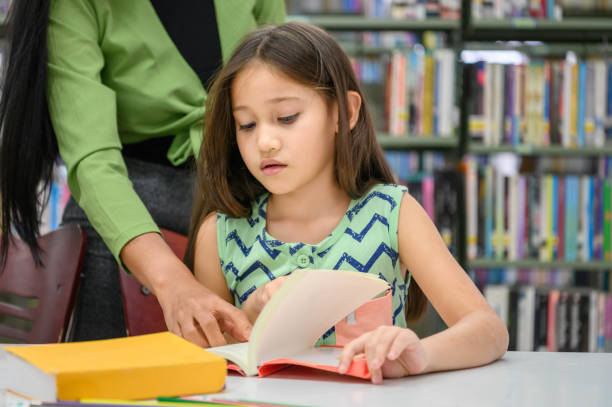istock Girl ask for teacher to answer question in book while reading book at school library. Education and learning concept. 1286144999