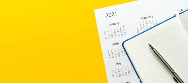 close up top view on white calendar 2021 schedule with blank notebook page and pen on yellow color background to make appointment meeting or manage timetable each day for design planning work and life concept