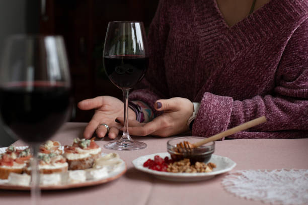 A gourmet lunch for two: a plate of dried cranberries and walnuts, a small bowl of honey, two glasses of wine, a plate with camambert cheese, fragrant baguette slices covered with cream cheese, smoky salmon and pieces of roquefort cheese. A bouquet of flo
