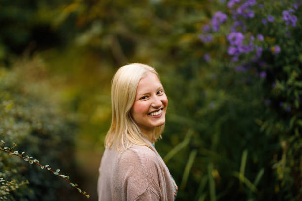 Woman in a blue top standing amidst hanging green vines, enjoying the serene beauty of nature in a garden setting.