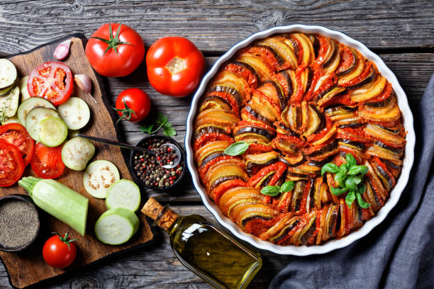 ratatouille, vegetable stew of sliced eggplant, zucchini, onion and potato with tomato sauce, ingredients at the background, french cuisine ratatouille, vegetable stew of sliced eggplant, zucchini, onion and potato with tomato sauce, ingredients at the background, french cuisine, horizontal view from above, flat lay ratatouille stock pictures, royalty-free photos & images