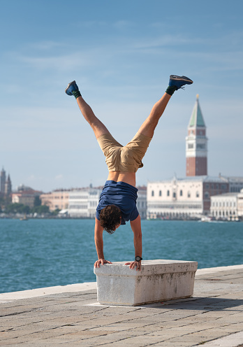 Athletic Man holding a yoga handstand on a stone bench in front of the famous Venice Skyline, Italy. Nikon D850. Converted from RAW.