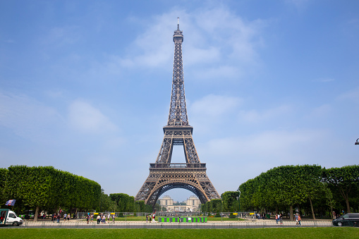 June 9, 2018 - Paris, France. A wide angle view of the Eiffel tower in Paris on a blue sky day with people walking through the park.