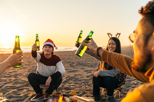 A group of young friends are celebrating Christmas outdoors at a beach during sunset.