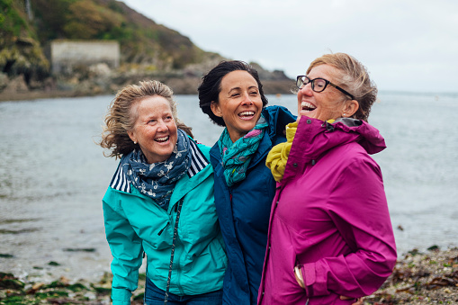 Friends and sisters exploring the outdoors together in Cornwall. They are standing with their arms around each other at the coast.