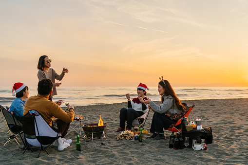 A group of young friends are enjoying a Christmas party at the beach and eating marshmallows.