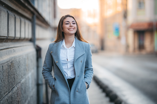 A smiling young woman in a gray coat. An ambitious look.