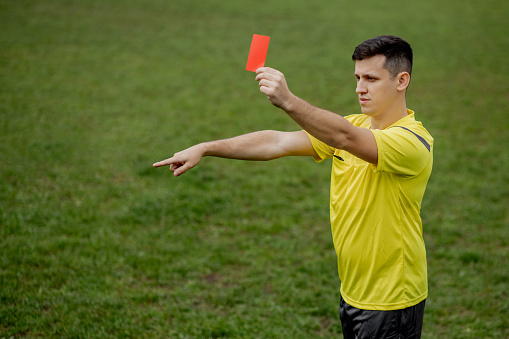 Angry football referee showing a red card and pointing with his hand on penalty.