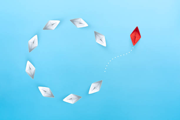 istock Group of white paper ships float in a circular direction and one red paper ship pointing in different way on blue background. Business for new ideas creativity, innovative and solution concept. 1286178769