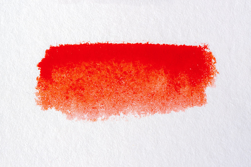 Macro image of dried red watercolour paint on a background of watercolour art paper.