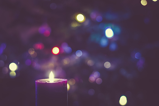 one burning candle concept with shining bokeh glittering ligts on christmas tree on background