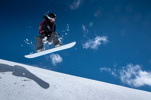 Young woman on a snowboard makes a flight after jumping from a snowy ledge against a dark blue sky high in the mountains in winter.