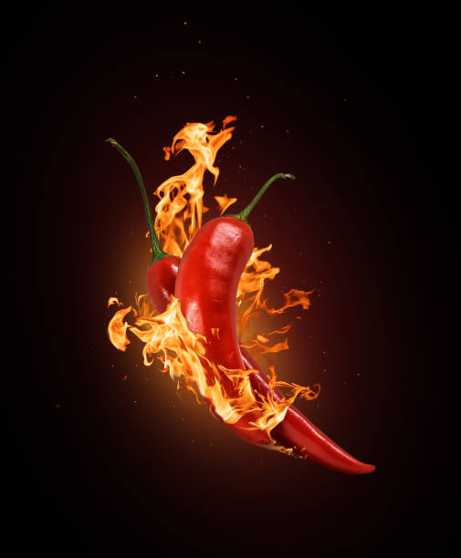 istock Two red chili peppers in a burning flame close-up on a black background. 1286183815