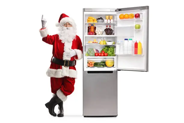 Photo of Full length portrait of santa claus leaning on a fridge and pointing up