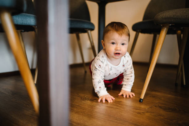 istock Adorable baby boy crawling underneath table. Real life toddler infant crawls under table at living-room or kitchen. Beautiful kid under the table. 1286187697