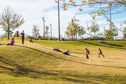 10-21-2018-Tulsa USA - Kids rolling down a grassy hill in unique urban public park - The Gathering Place - in Oklahoma - motion blur