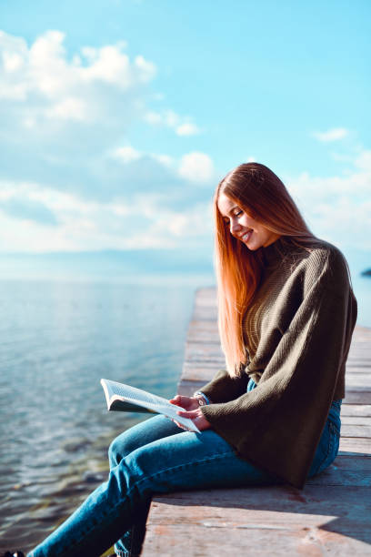 istock Beautiful Female Reading Book On Lake Pier 1286189540