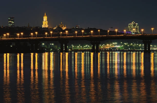 istock Night cityscape with Paton bridge over Dnieper river. Light from lanterns reflected in the water. Illuminated Bell tower of Kyiv Pechersk Lavra at the background. City lights reflected in the water 1286199585